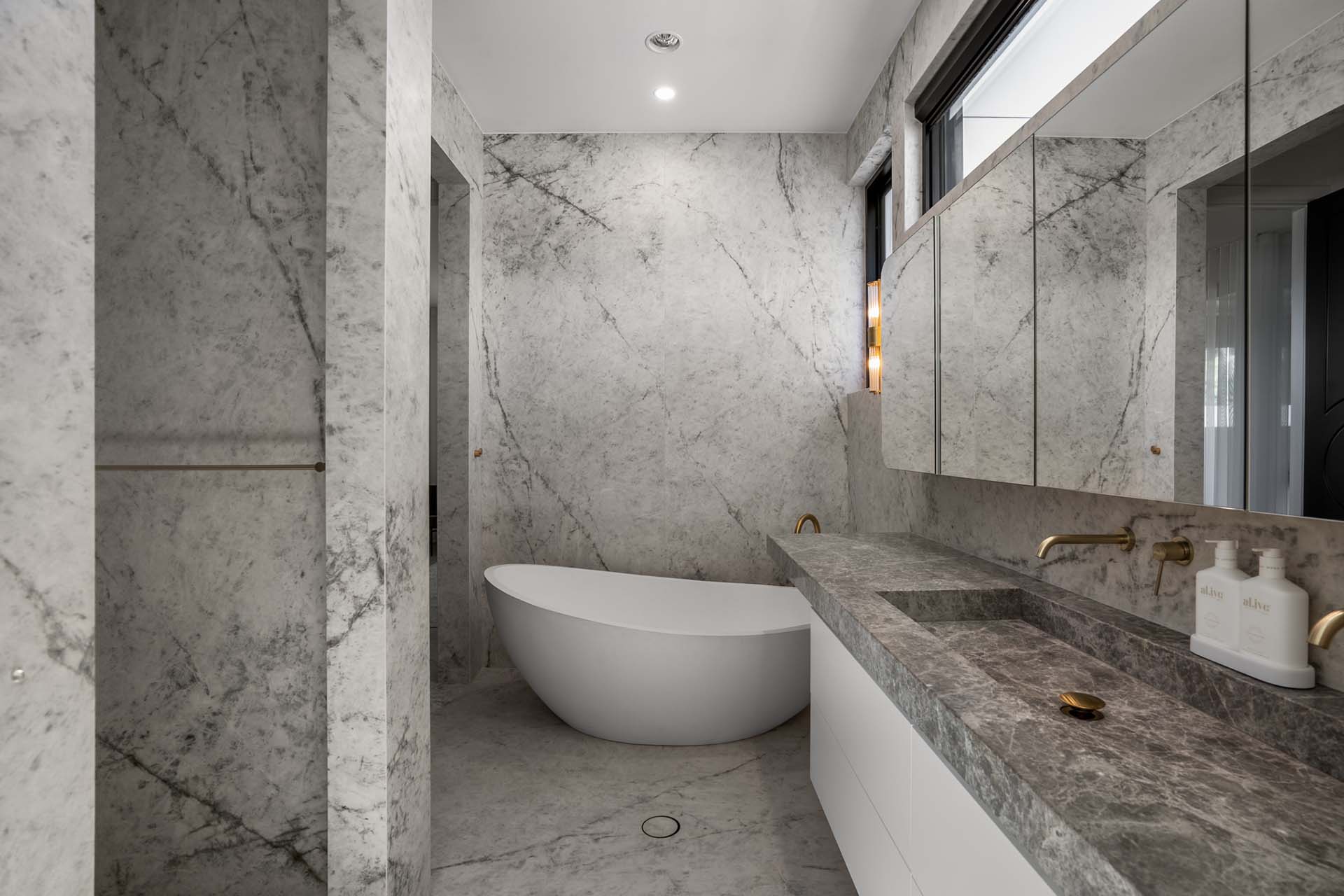 Marble bathroom design with Lorde White marble wall cladding, integrated stone basin, and bathtub. Gold tap ware