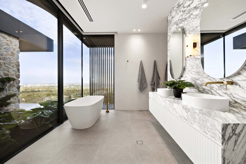 Luxurious bathroom with marble vanity, freestanding tub, and floor-to-ceiling glass walls overlooking a cityscape.