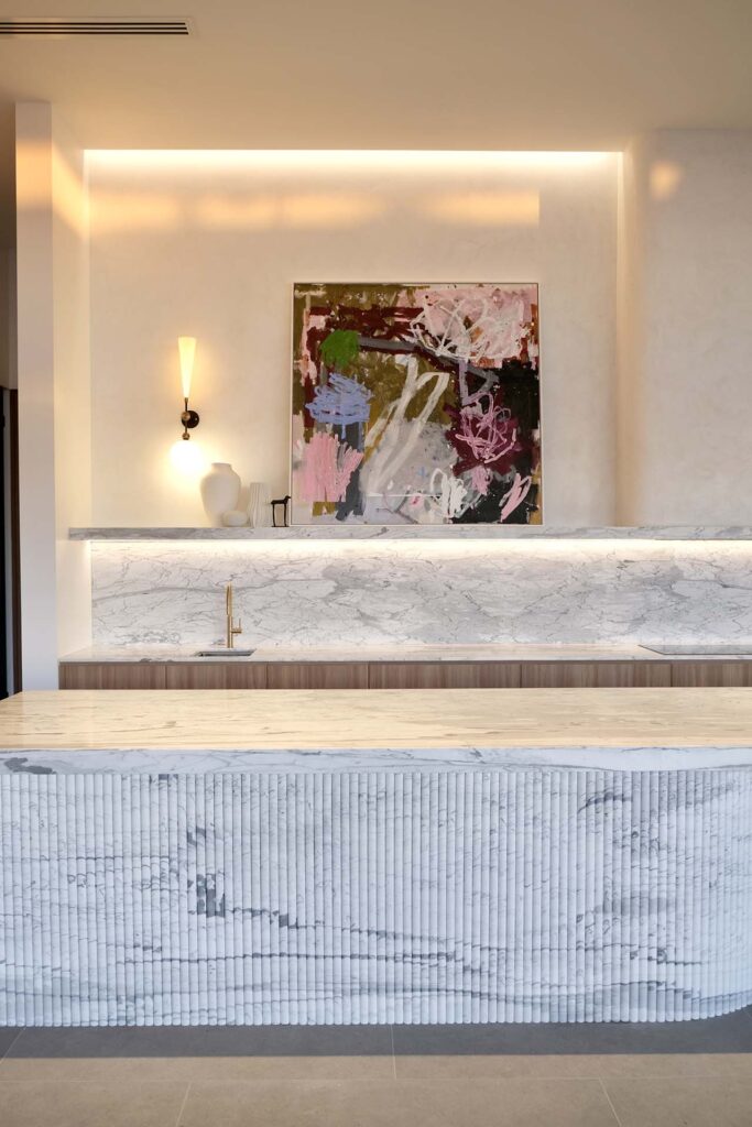 Modern kitchen area with marble counters and backsplash, ribbed island front, and an abstract painting on the wall.