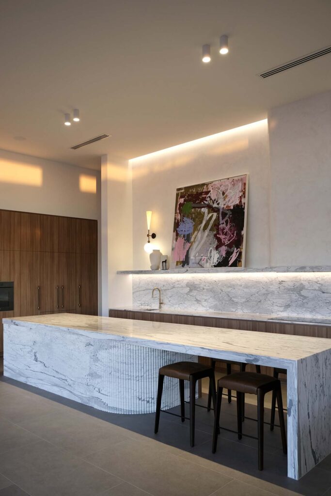 Modern kitchen with a white marble island, wood cabinets, and a colorful abstract painting on the wall
