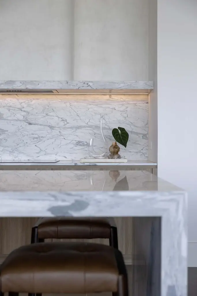Modern marble kitchen with a marble backsplash, a glass sculpture, and a small plant on the counter.
