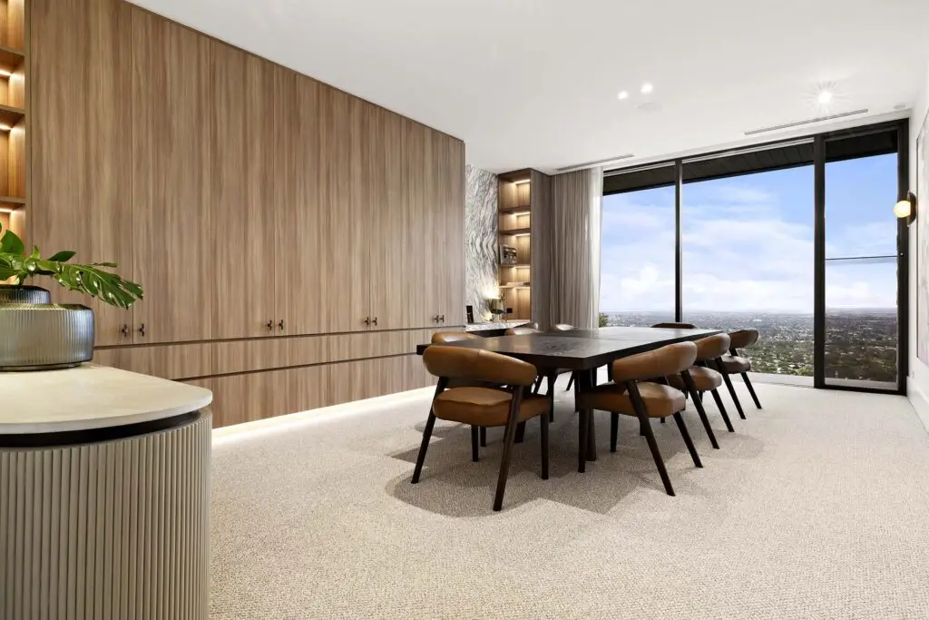 Modern dining room with full-height wooden cabinetry, a dark wood dining table and brown leather chairs, and a panoramic city view through large windows.