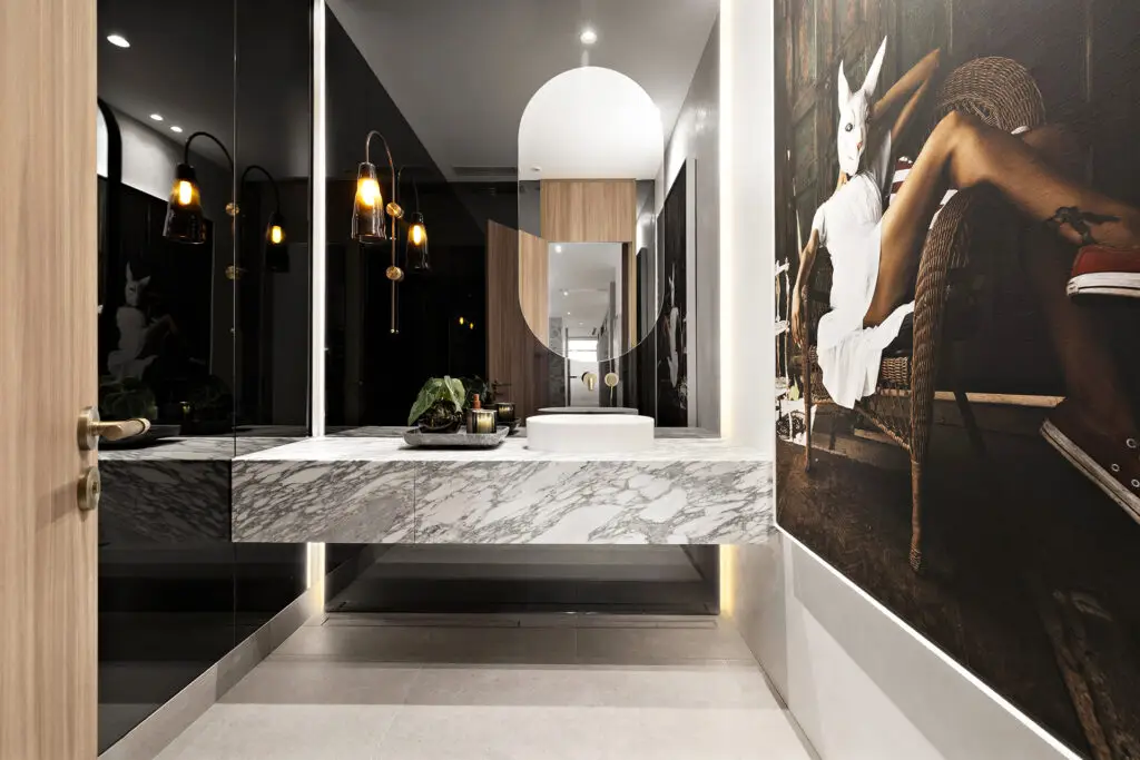Modern bathroom with a marble vanity, round white sink, and a circular mirror, plus warm amber pendant lights.
